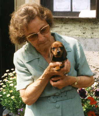 Eine ältere Dame mit großer Sonnenbrille hält einen braunen Dackelwelpen in den Armen