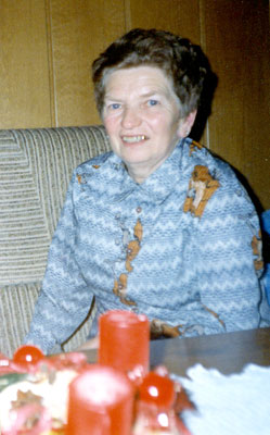 Portrait einer älteren Dame die milde lächelnd auf einer Couch sitzt, vor ihr ein Adventkranz