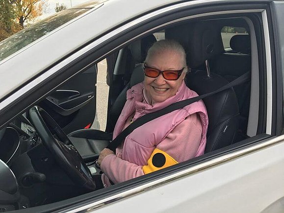 Seniorin in rosa Weste und Pullover sitzt angeschnallt in einem weißen Auto