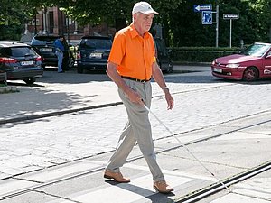 Blinder Mann geht mit einem Taststock über einen Zebrastreifen.