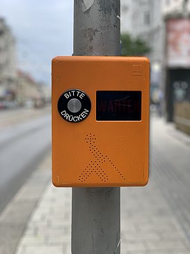 Akustikampel orange mit Bitte-drücken Knopf und Piktogramm einer blinden Person