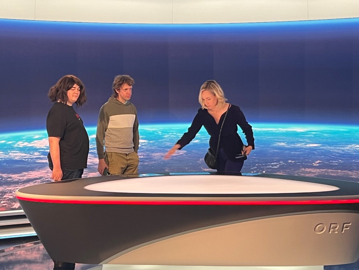 Moderatorin Nadja Bernhard erklärt zwei Personen etwas im Nachrichtenstudio der Zeit im Bild.