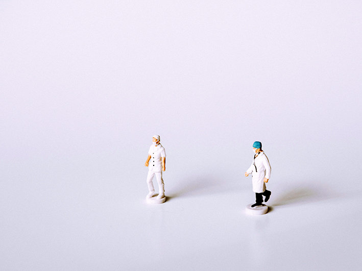Zwei kleine Figuren in Form von Ärzt:innen auf weißem Hintergrund