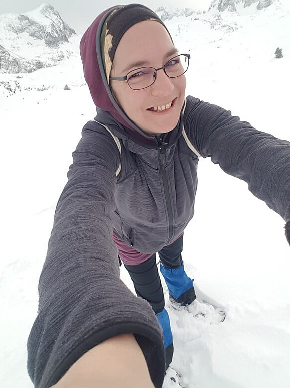 Eine Frau mit Schneeschuhen und Winterbekleidung ist in den Bergen unterwegs.