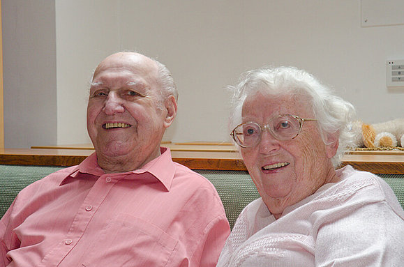 Ein älteres Ehepaar sitzt einander zugeneigt lachend nebeneinander