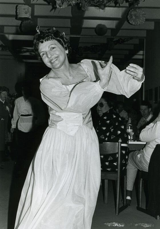 Lygia Kapraleck tanzend mit erhobenen Armen und lächelnd, trägt ein weißes Kleid mit Puffärmeln (Silvester 1988)