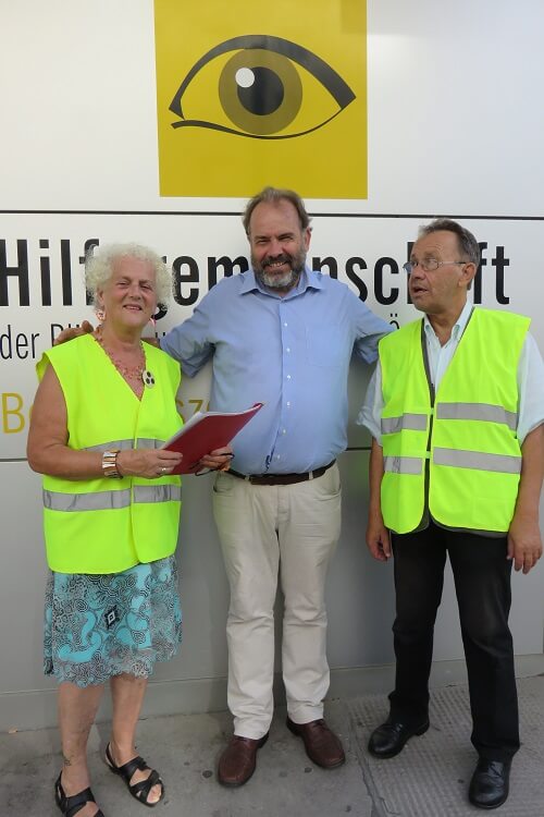 Hubert Wagner posiert mit „Ampelpaten“ Veronika Kerschbaum und Michael Watz lächelnd für ein Foto vor dem Eingang der Hilfsgemeinschaft.