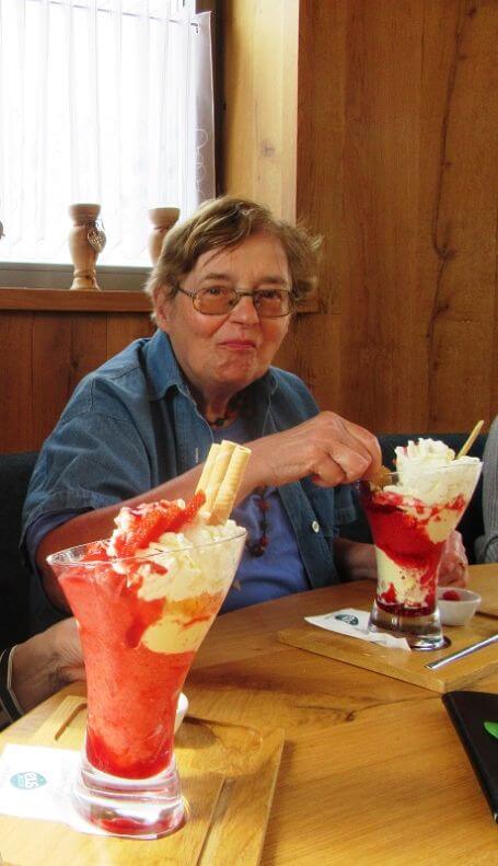 Seniorin sitzt vor einem Tisch mit zwei großen Erdbeereisbechern.