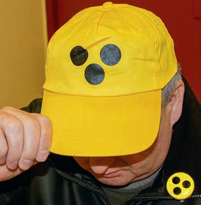 Eine gelbe Schirmmütze mit 3 schwarzen Punkten wird von einem Mann auf dem Kopf getragen.