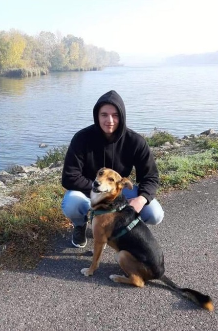 Mann mit Kapuzenpulli und Hund vor einem Fluss