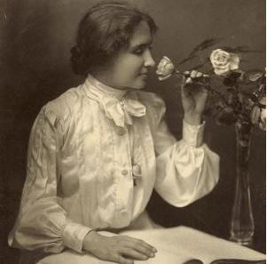 bräunliches Schwarzweiß-Foto: Junge Frau mit weißer Bluse berührt mit einer Hand Buchseiten und mit anderen riecht sie an einer Rose