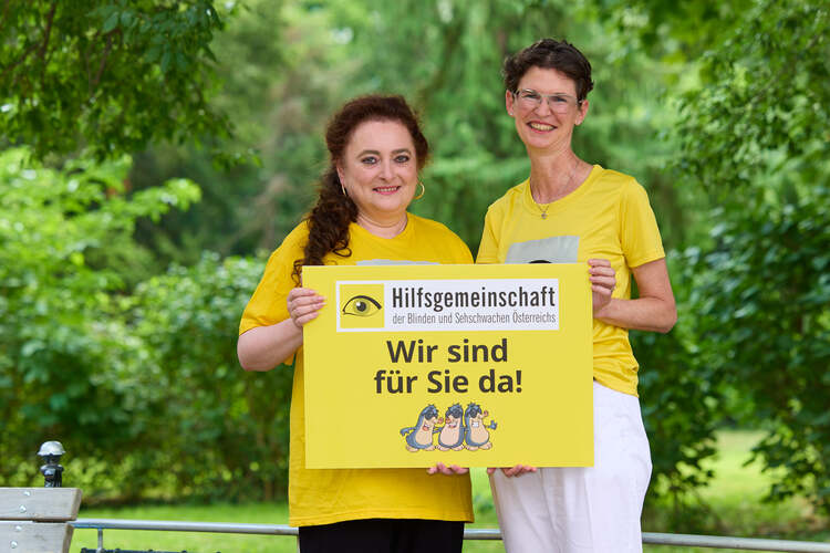 Zwei Frauen in gelben Shirts stehen vor Büsche