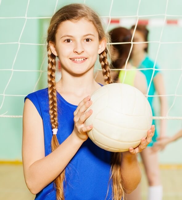 Ein Teenager-Mädchen in blauem, ärmellosen Shirt und mit Zöpfen, hält einen Volleyball in die Höhe.