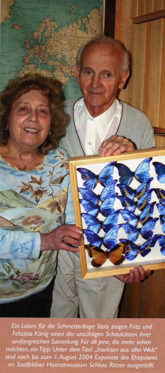 Ein älteres Ehepaar steht nebeneinander und hält lächelnd einen Schaukasten mit seltenen blauen Schmetterlingen in die Kamera. 
