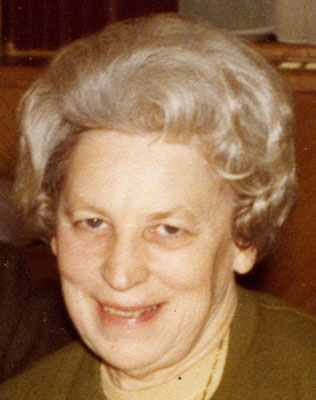 Eine ältere Dame mit weißer Dauerwelle lächelt verschmitzt 