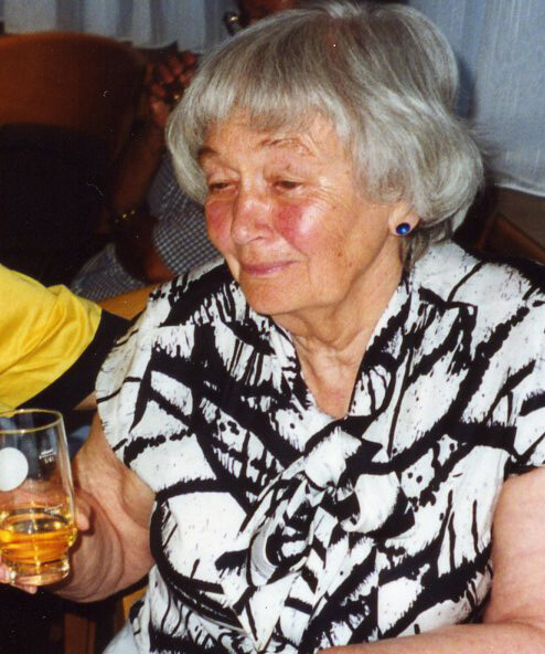 Ältere Dame lächelt milde, hält ein Glas Apfelsaft in der Hand.