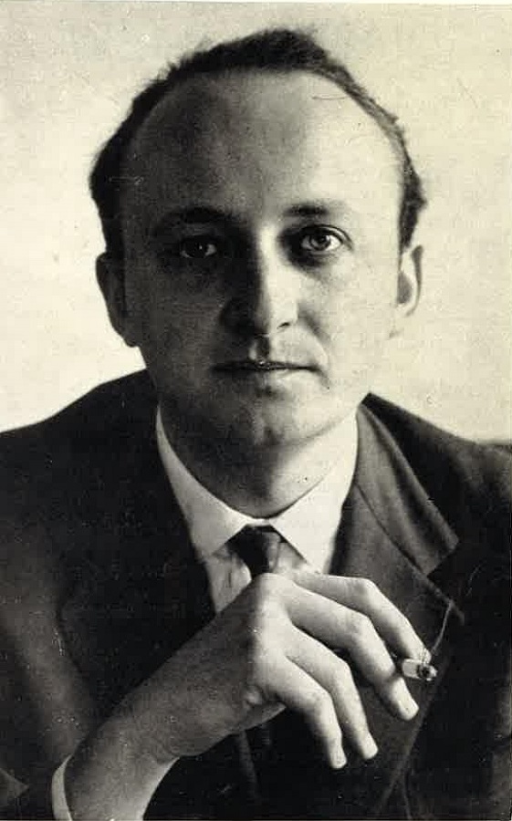 Schwarz-Weiß-Foto, ein Mann blickt mit ernstem Gesicht in die Kamera, er trägt einen Anzug und hält eine Zigarette in der Hand