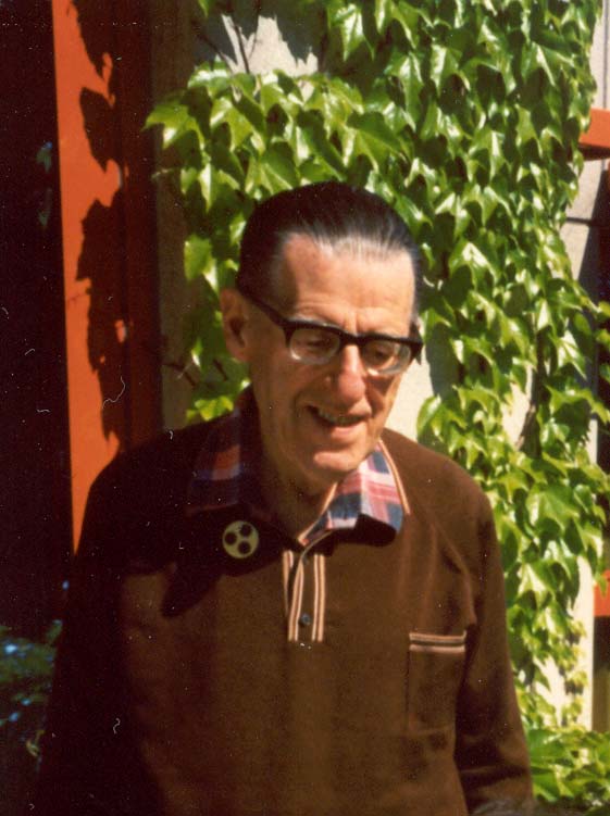 Älterer Herr mit Brille und Anstecknadel vor einer mit wildem Wein bewachsenen Hauswand