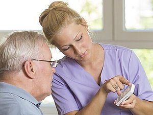 Pflegerin zeigt einem älteren Mann die Medikamentendose.
