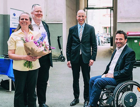 eine Frau mit Blumenstrauß und drei Männer lächeln in die Kamera