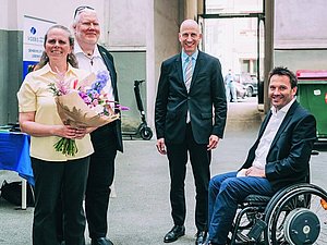 eine Frau mit Blumenstrauß und drei Männer lächeln in die Kamera