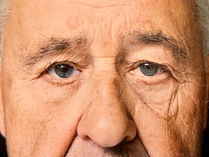 Ein Gesicht eines älteren Mannes mit blauen Augen und grauen Haaren.