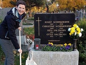Alexandra Masetti steht mit einem Besen bei einem Grab