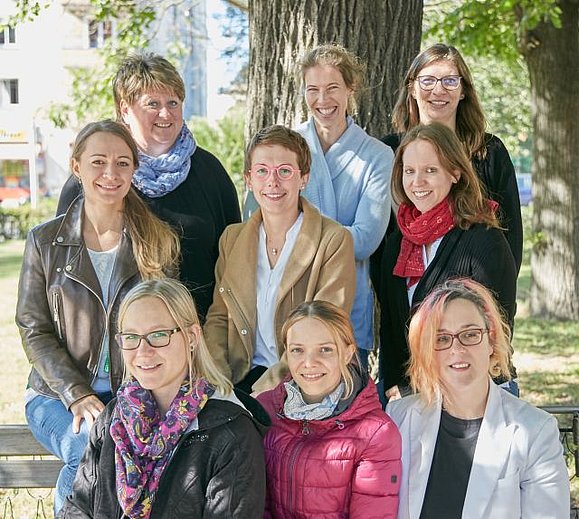 9 Frauen stehen zusammen im Park.