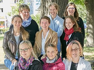 9 Frauen stehen zusammen im Park.