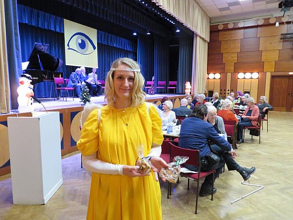 Eine junge Frau ist als Christkind verkleidet: Mit gelbem Kleid und weißen Flügeln.