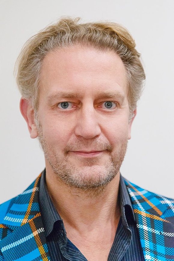 Porträt: Mann mit Bart und blonden kurzen krausen Haaren trägt Blau-kariertes Jacket