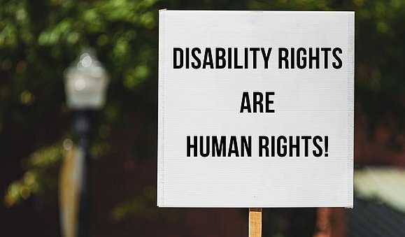 Protestschild vor Baum: "DISABILITY RIGHTS ARE HUMAN RIGHTS!"