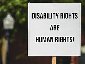 Protestschild vor Baum: "DISABILITY RIGHTS ARE HUMAN RIGHTS!"