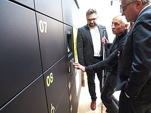 Mann mit Langstock berührt Display an Wand mit Paketboxen