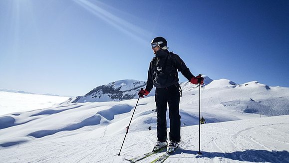 Mensch auf Skiern in Schneelandschaft, blauer Himmel.