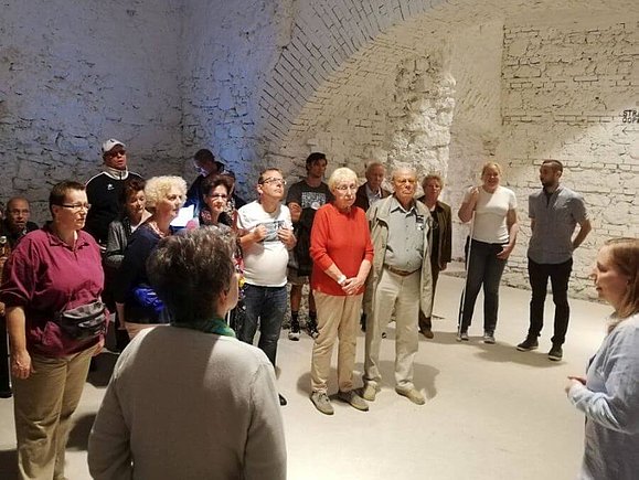 16 Personen hören gespannt der Museumsführerin zu.