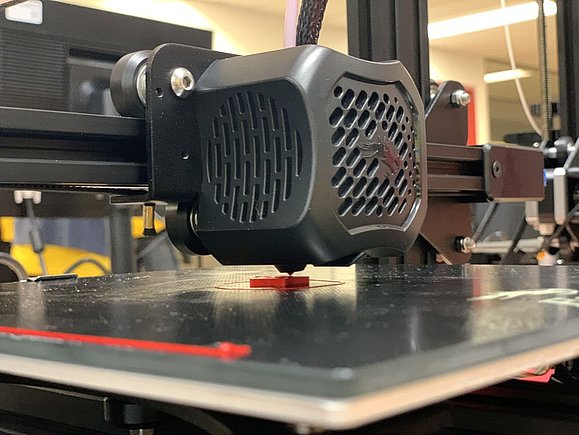 3D Drucker beim Drucken mit rotem Plastik auf schwarzer Oberfläche