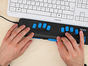 Zwei Hände auf einer Braille-Tastatur
