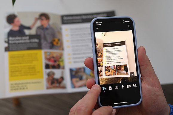 Smartphone im Fokus mit Vorleseapp, die gerade Infobroschüre mit der Kamera zoomt