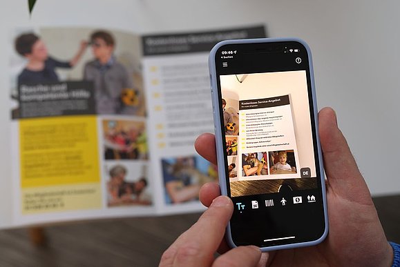 Smartphone im Fokus mit Vorleseapp, die gerade Infobroschüre mit der Kamera zoomt