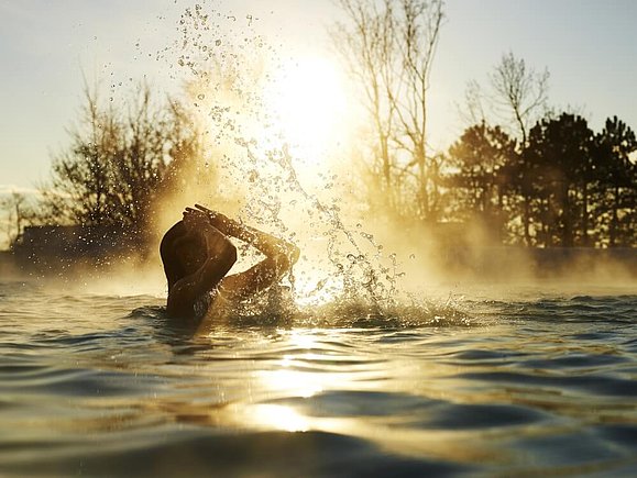 Eine Frau badet im Thermalbecken vor dem Sonnenuntergang