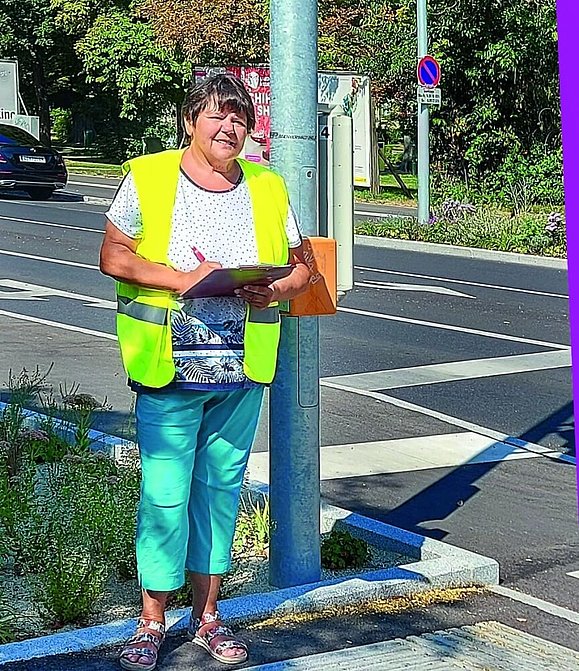 Frau mit gelber Warnweste und Schreibzeug steht neben Akustikampel