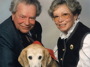 Foto eines älteren Ehepaares mit einem Hund in der Mitte. 