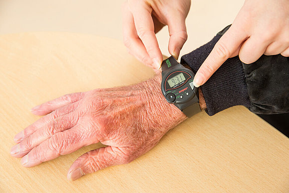 Zeigefinger auf der Taste zur Ansage der Uhrzeit an einer sprechenden dunkelgrauen Armbanduhr an einem Handgelenk. Copyright: Franz Pfluegl