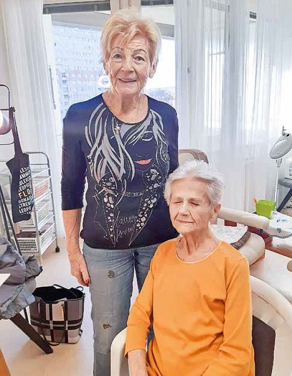 Zwei ältere Frauen, eine sitzt, in einem Pflegezimmer.