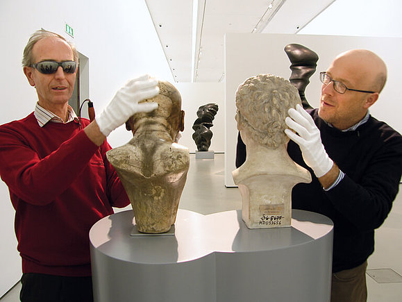 Sehbeeinträchtigte Besucher betasten mit weißen Handschuhen Büsten von Franz Xaver Messerschmidt