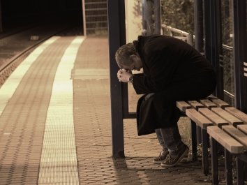Ein verzweifelter Mann sitzt traurig und einsam an einer Haltestelle.