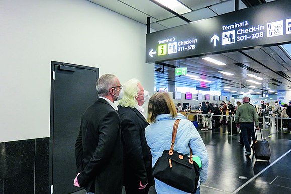 Drei Personen schauen auf eine Anzeigentafel am Flughafen.