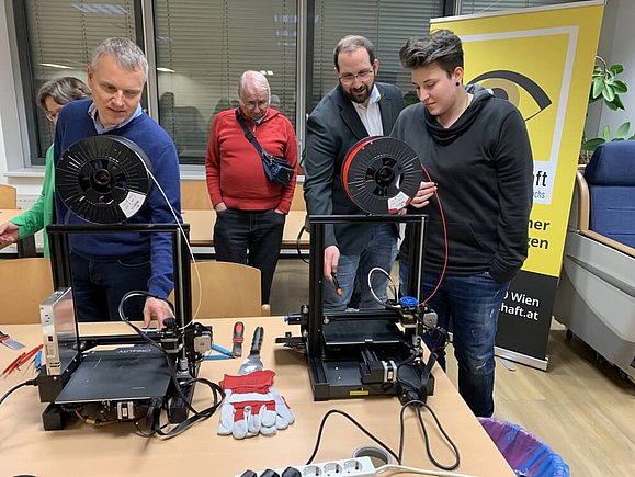 mehrere Leute vor 2 schwarzen 3D-Druck-Geräten