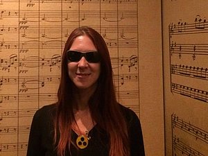 Frau mit Sonnenbrille steht vor Wänden auf denen Musiknoten geschrieben sind